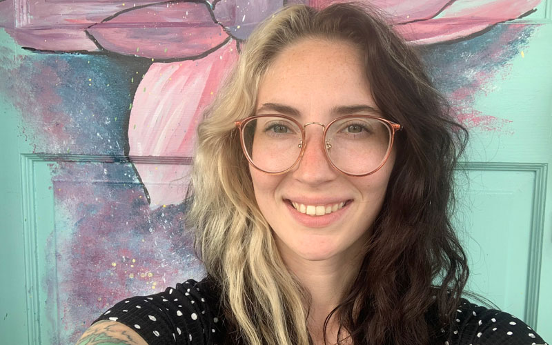 Stephanie Condit wearing a black shirt with polka dots in front of a green door with flowers painted on it