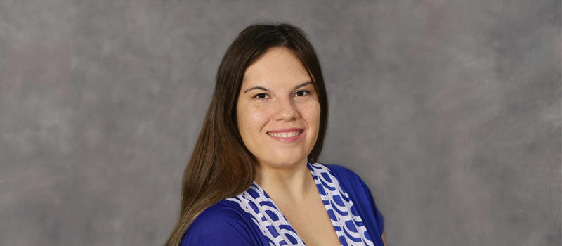 Nicole Rabalais wearing a blue dresss with spotted lapels in front of a grey mottled background